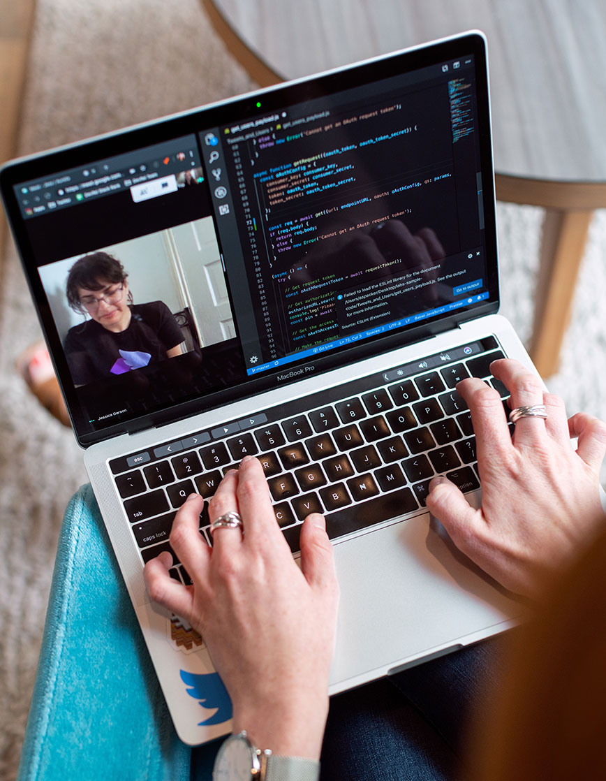 Person Working on Laptop 2 Person typing code on a MacBook Pro showing a split screen with a video call on the left and code editor on the right.