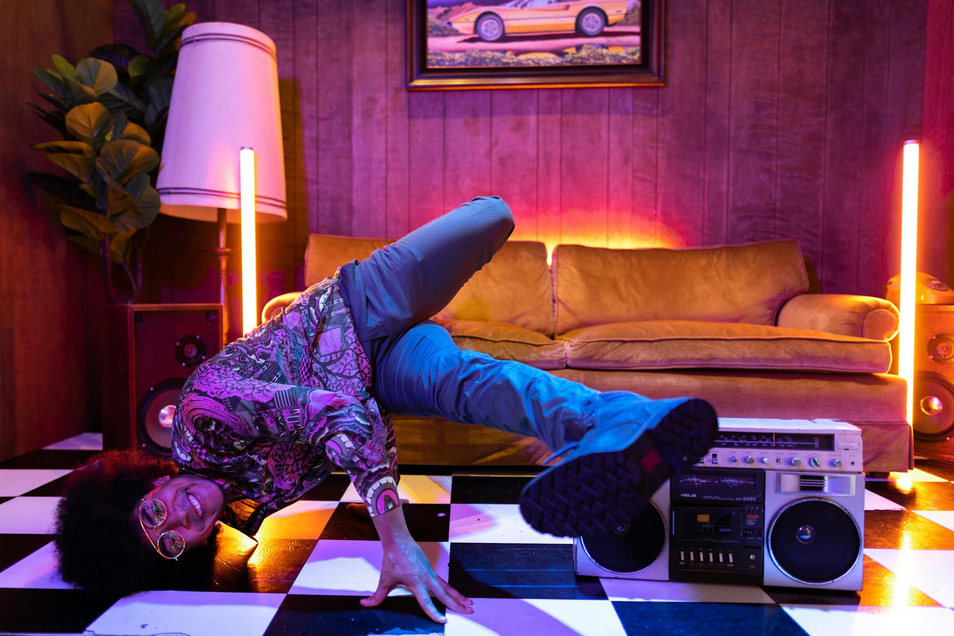 flexible-guy-break-dancing Person breakdancing on a black-and-white checkered floor in a retro-lit room, one hand on the floor, vintage boombox nearby.