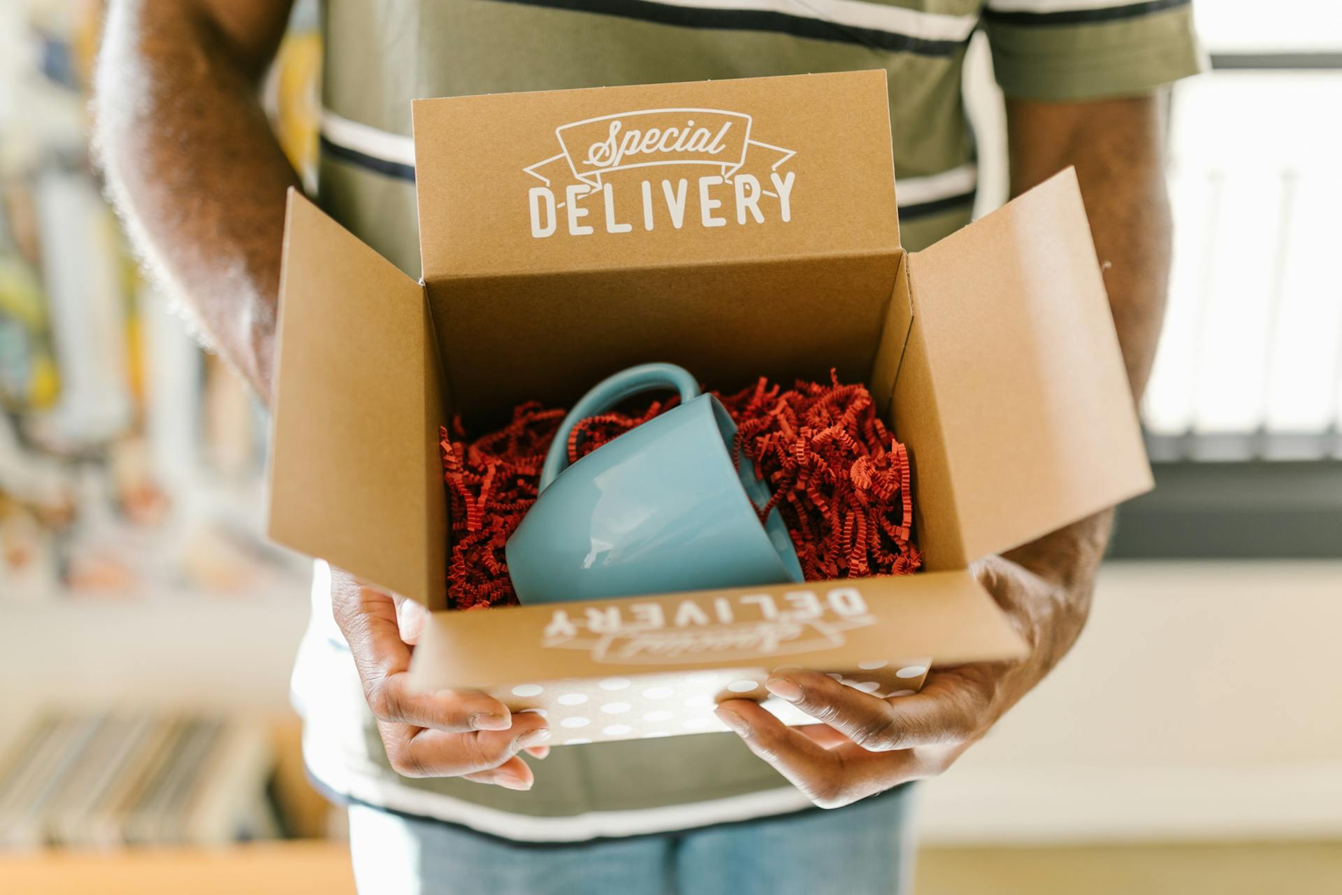 man-holding-box-containing-mug Person holding an open "Special Delivery" box with red paper filler and a blue ceramic mug inside