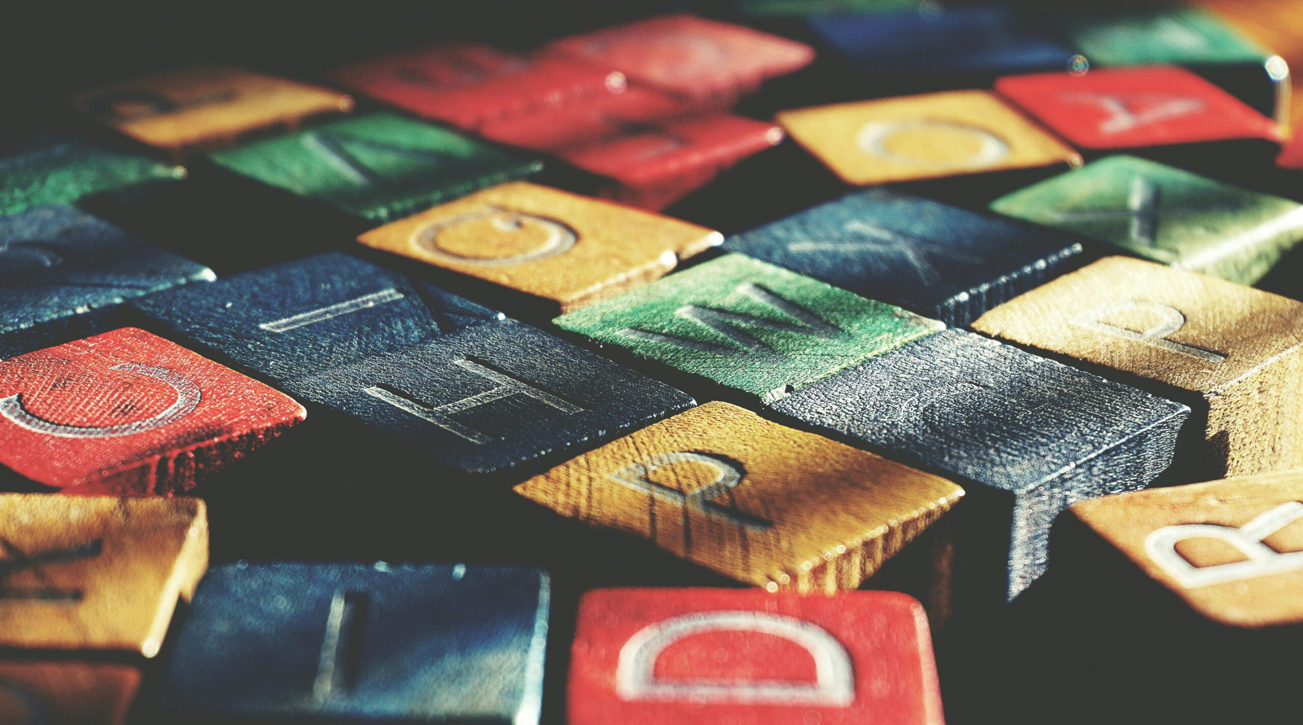 Close-up of colorful wooden alphabet tiles stacked in rows, showing letters like D, O, W and textured painted surfaces
